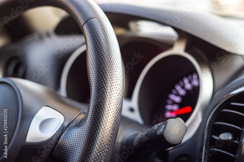 Close up modern black steering wheel, blurred dashboard, key and speedometer. Selective focus. Shallow depth of field.