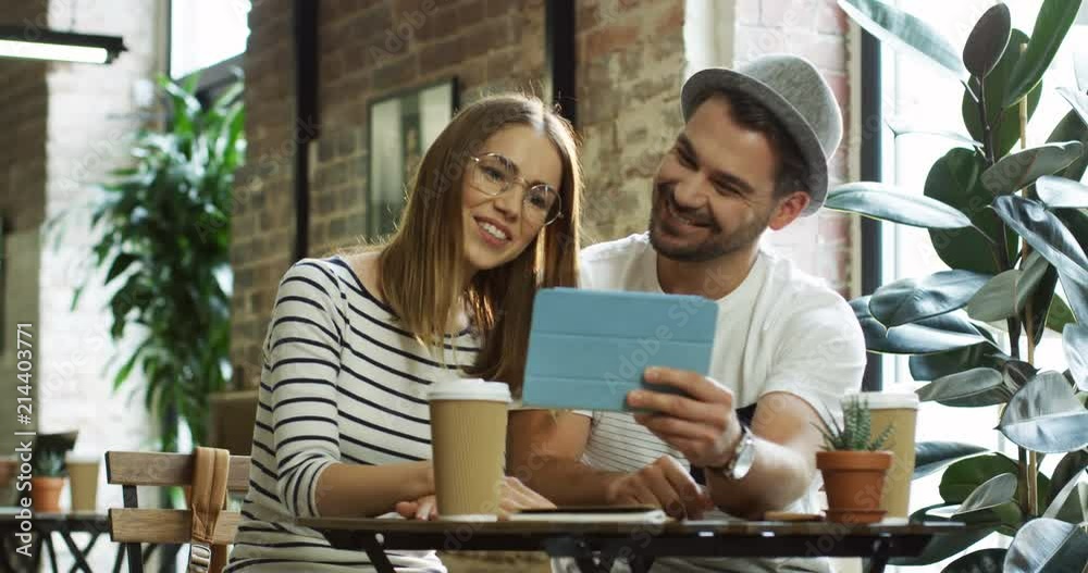 Young cheerful caucasian couple sitting at the loft cafe and having videochat on the tablet device.