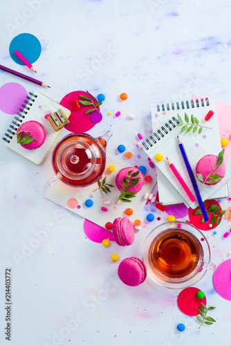 Glass teapot with candies and confetti on a light background with copy space. Pink and purple palette still life. Vibrant tea party drinks flat lay.