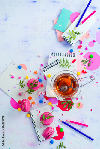 Drinking tea and working concept. Tea cup, teapot, notepads with blank pages, candies and confetti from above. Planning and creative work still life with copy space