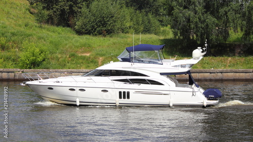 Travel, luxury water recreation on boat - a white 58-ft motor yacht slowly floating along the concrete shores of the navigable canal in summer amid the green trees on the shore, side view