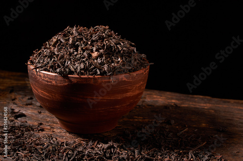 Dry tea leaves in clay bowl on black background. selective focus