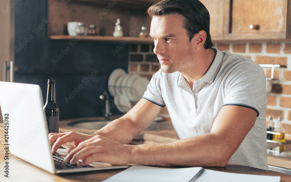 Remote job. Serious nice smart man sitting at the laptop and typing while working at home Remote job. Serious nice smart man sitting at the laptop and typing while working at home