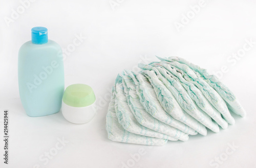 Baby diapers on a white background and baby shampoo and cream