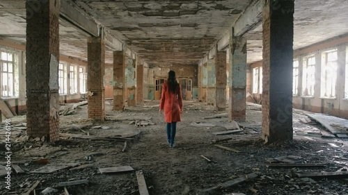 Unrecognizable woman in a red cloak inspects destroyed building after the disaster earthquake, flood, fire.