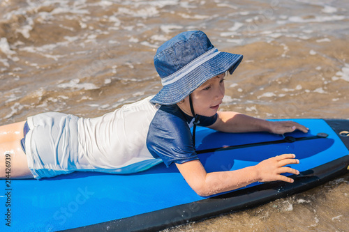 Happy baby boy - young surfer ride on surfboard with fun on sea waves. Active family lifestyle, kids outdoor water sport lessons and swimming activity in surf camp. Summer vacation with child photo