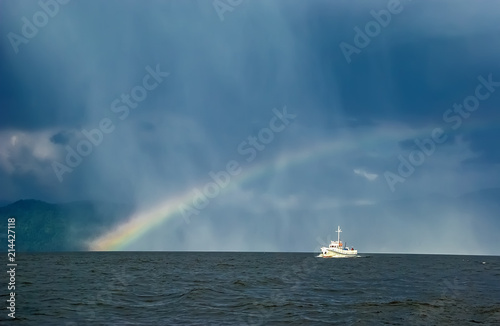 boat sailing along a mountain lake against the background of rain and rainbow