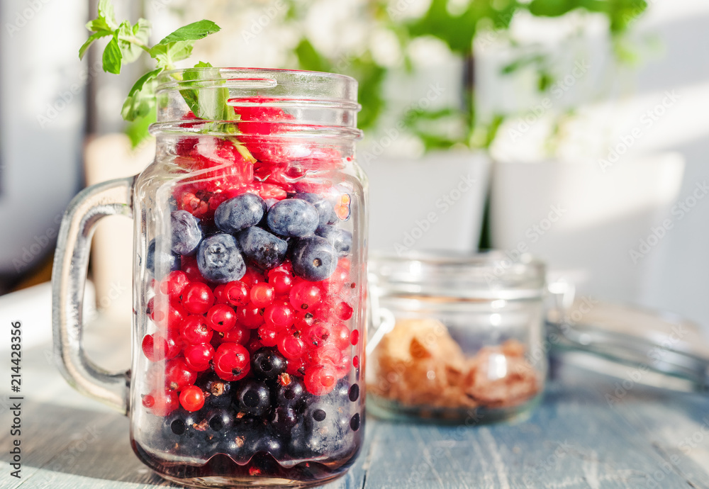 A glass jar with different fresh summer berries is on the table, a healthy breakfast, a diet, detox, summer treats A glass jar with different fresh summer berries is on the table, a healthy breakfast, a diet, detox, summer treats