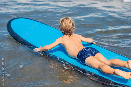 Happy baby boy - young surfer ride on surfboard with fun on sea waves. Active family lifestyle, kids outdoor water sport lessons and swimming activity in surf camp. Summer vacation with child photo