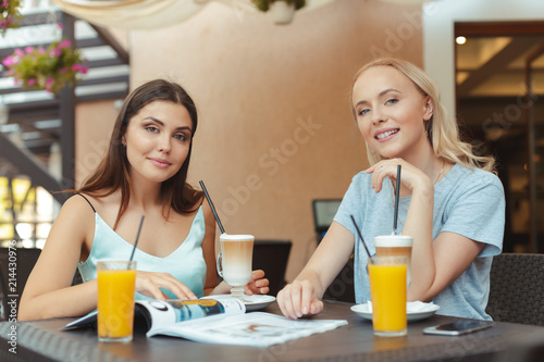 Two beautiful young girls sitting by the table in cafe