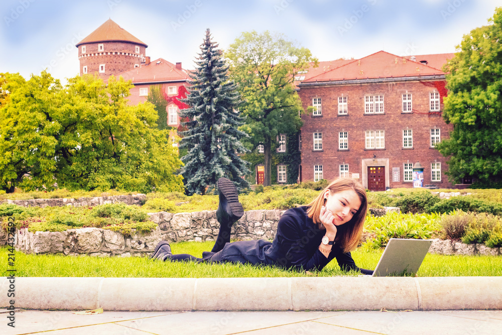 Girl student with a laptop on a lawn in front of universities