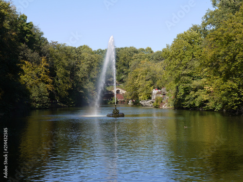 a high jet of fountain from the mouth of a snake is sprayed along the surface of a large lake in the park photo