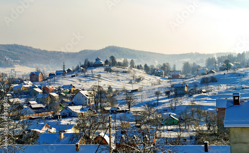 Rural settlement with small snow-covered houses, yards and a church on a hill