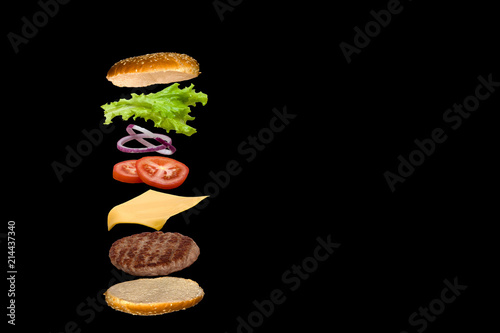 Obraz na plátně Delicious burger with flying ingredients isolated on black background
