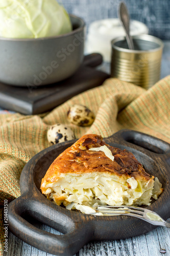 A slice of homemade pie with cabbage on a round wooden plate on an old table. 