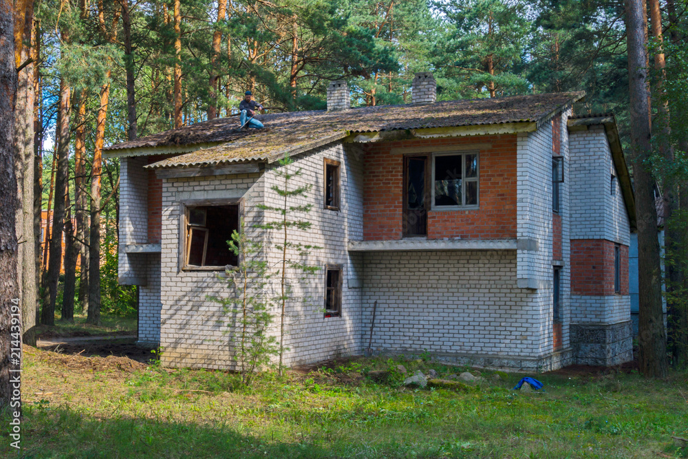 Unfinished brick two-storey house in the background of a pine forest
