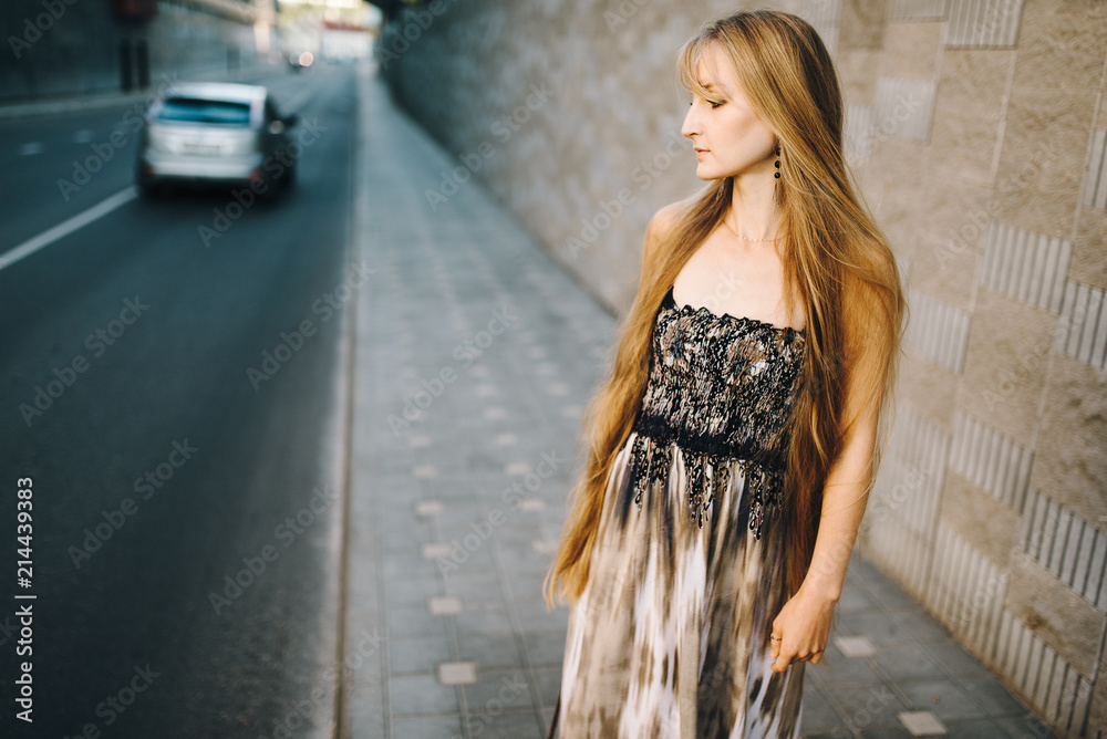 Attractive young girl with long hair walking down the street against the background of an old building. Her long dress and hair flew from the wind and moved.