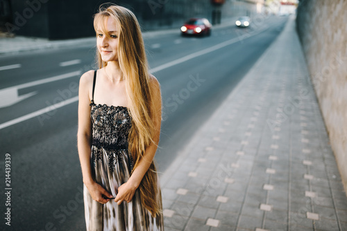 Attractive young girl with long hair walking down the street against the background of an old building. Her long dress and hair flew from the wind and moved.