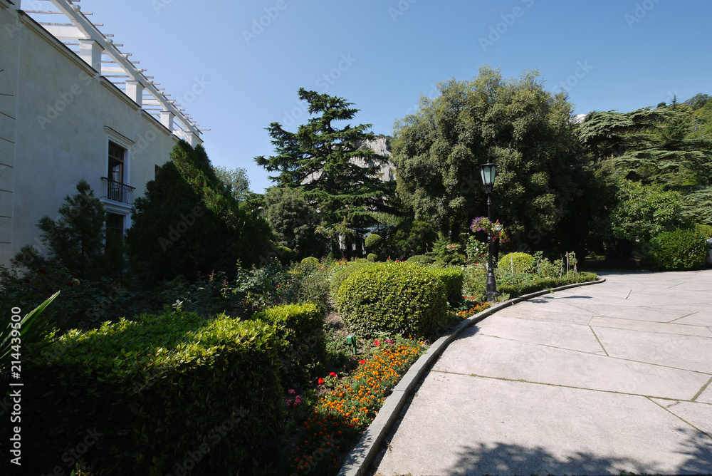 Obraz premium Picturesque green vegetation in the park near the path with designer bushes growing next to them flowers and lush trees.