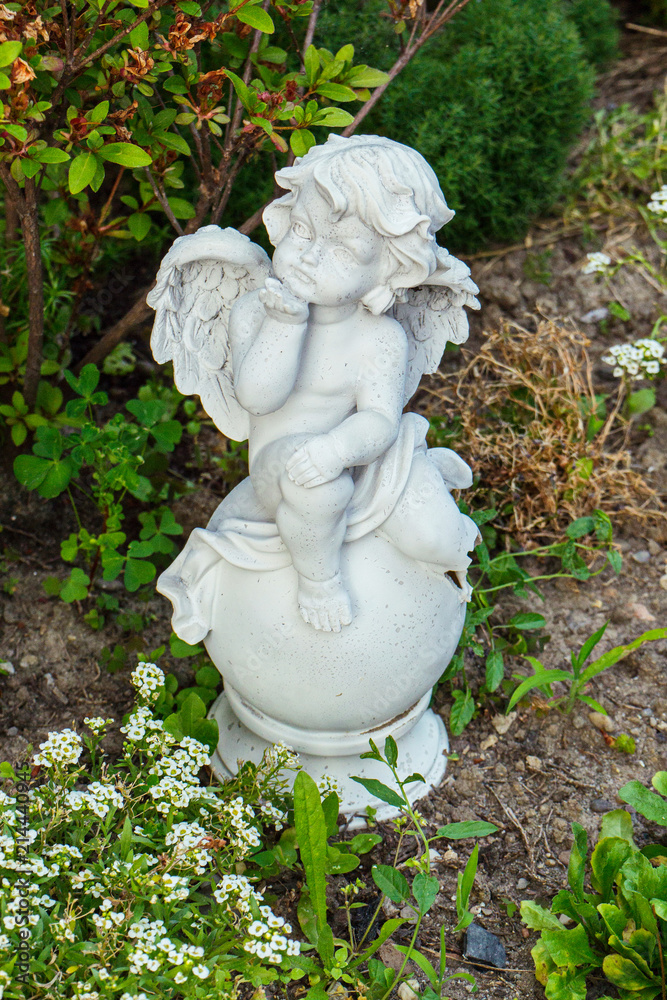 white statue of a small angel on a ball near a bush of a delicate and fragrant flower alisium white statue of a small angel on a ball near a bush of a delicate and fragrant flower alisium