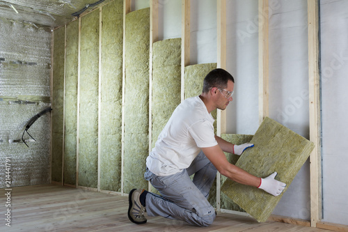 Worker in protective goggles and respirator insulating rock wool insulation in wooden frame for future house walls for cold barrier. Comfortable warm home, economy, construction and renovation concept photo