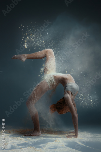 Dancing in flour concept. Redhead beauty gymnast female girl adult woman dancer in dust   fog. Girl wearing white top and shorts making dance element in flour cloud on isolated grey background
