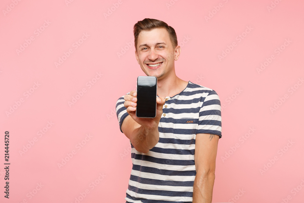 Portrait of man in striped t-shirt showing mobile phone camera with blank black empty screen copy space isolated on trending pastel pink background. People sincere emotions concept. Advertising area. Portrait of man in striped t-shirt showing mobile phone camera with blank black empty screen copy space isolated on trending pastel pink background. People sincere emotions concept. Advertising area.