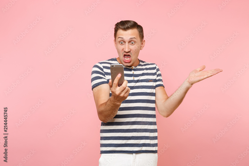 Portrait of sad angry shocked young man looking on display mobile phone, surprised sms You're fired, dismissal from work isolated on pastel pink background. People sincere emotions lifestyle concept.