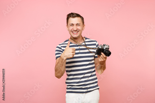 Portrait of smiling young photographer man wearing striped t-shirt take pictures on retro vintage photo camera isolated on trending pastel pink background. People sincere emotions lifestyle concept.
