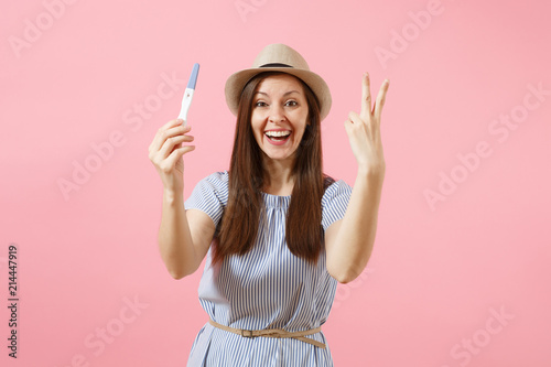 Принти на полотні Excited happy woman in blue dress, hat hold in hand, looking at pregnancy test isolated on pink background