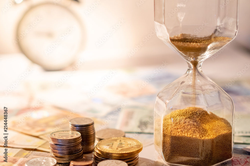 Sand running through the shape of hourglass on table with banknotes and coins of international currency. Time investment and retirement saving. Urgency countdown timer for business deadline concept
