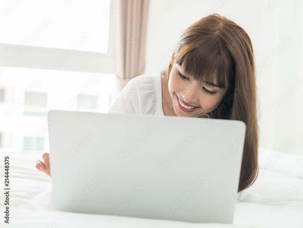 Happy casual beautiful asian woman lying on bed using laptop in bedroom at home Happy casual beautiful asian woman lying on bed using laptop in bedroom at home