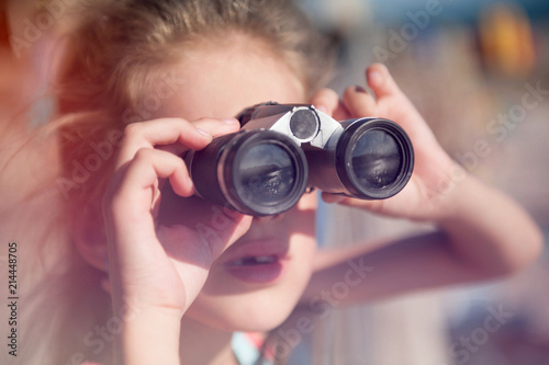 cute little caucasian girl holding binoculars watching sea and mountains