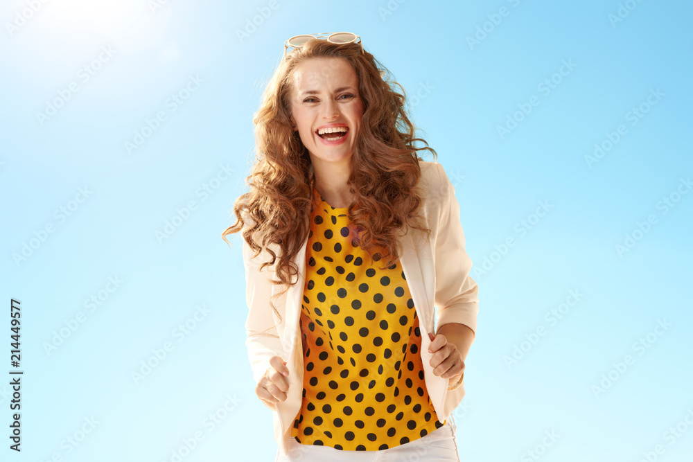 cheerful stylish woman in light jacket against blue sky