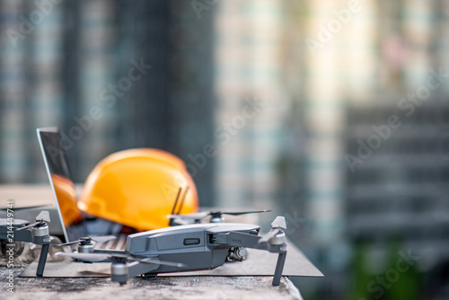 Drone, laptop computer and protective helmet at construction site. Using unmanned aerial vehicle (UAV) for land and building site survey in civil engineering project.