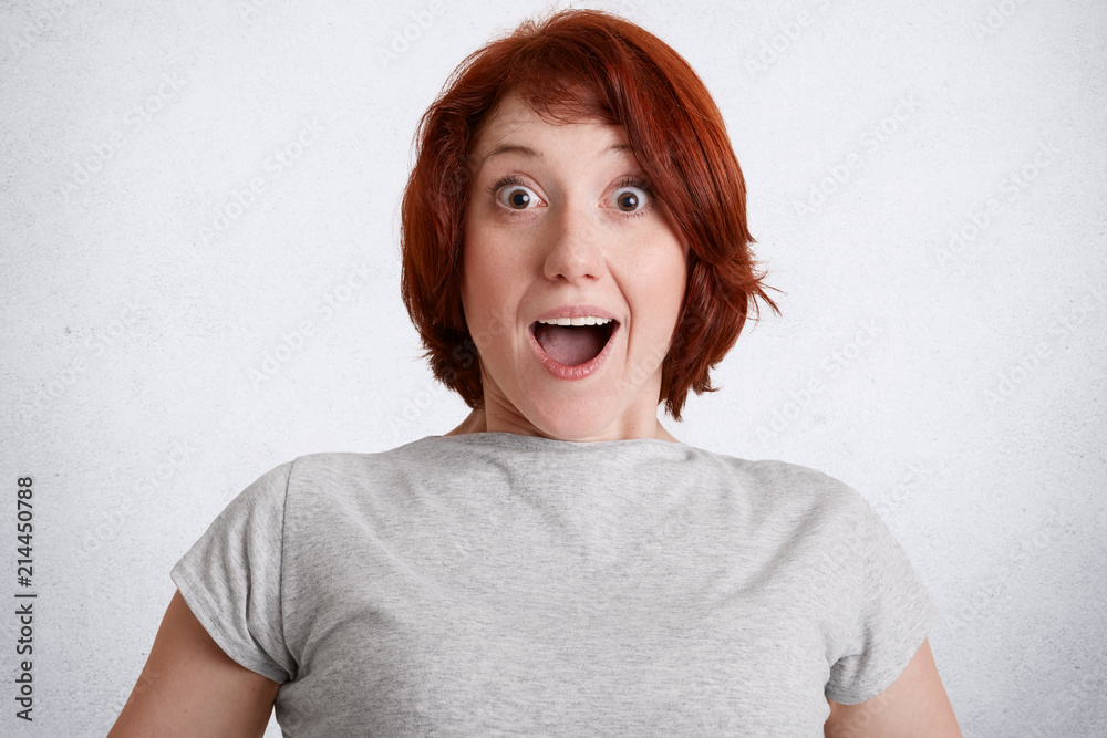 Astonished ginger female with shocked facial expression, stares with ...