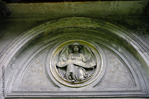 A weathered sandstone relief of an angel in front of a crypt. photo