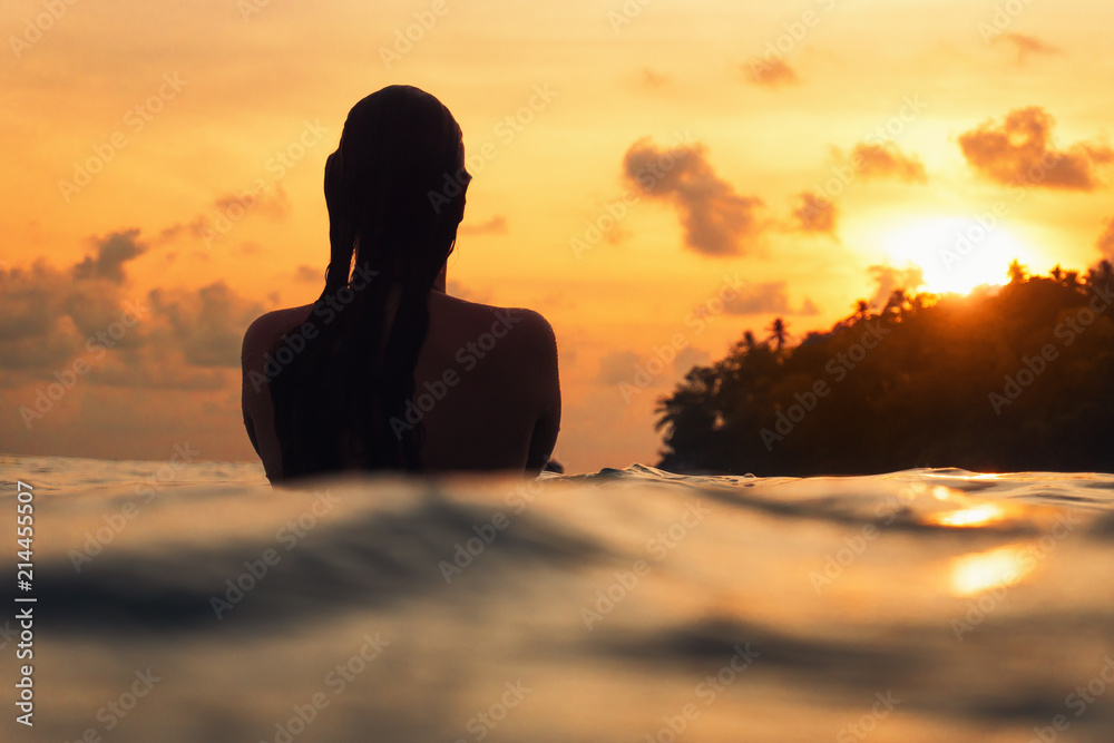 Obraz premium young woman from behind in indian ocean during orange sunset with romantic mood