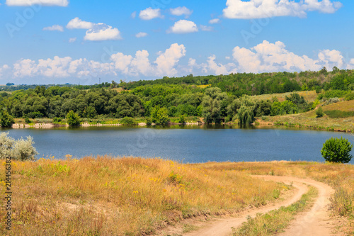Summer landscape with dirt road to the lake and blue sky with white clouds