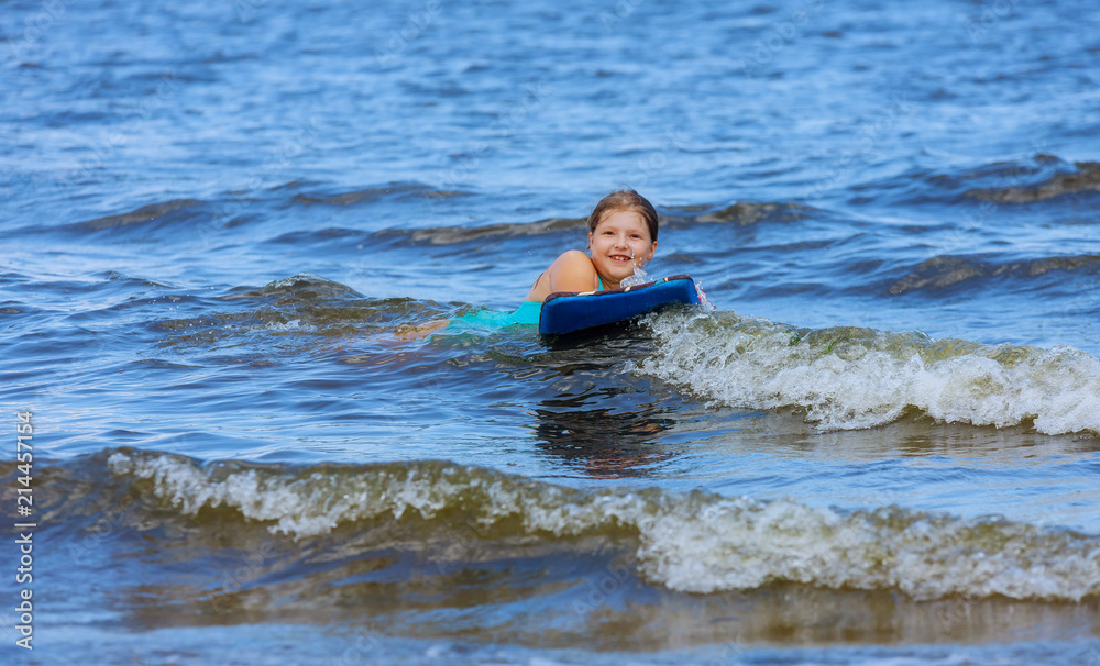 Adorable little baby girl young surfer with bodyboard a fun on small ocean waves.