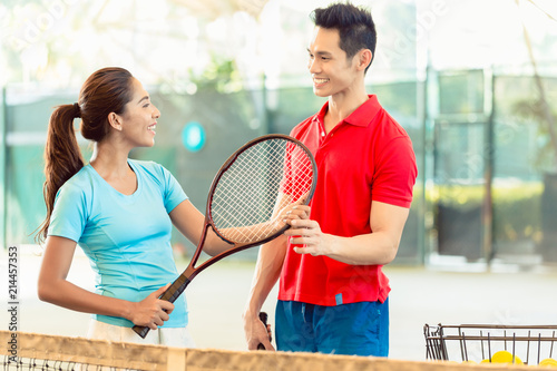 Fotografie Chinese tennis instructor smiling while teaching a beginner female player the co
