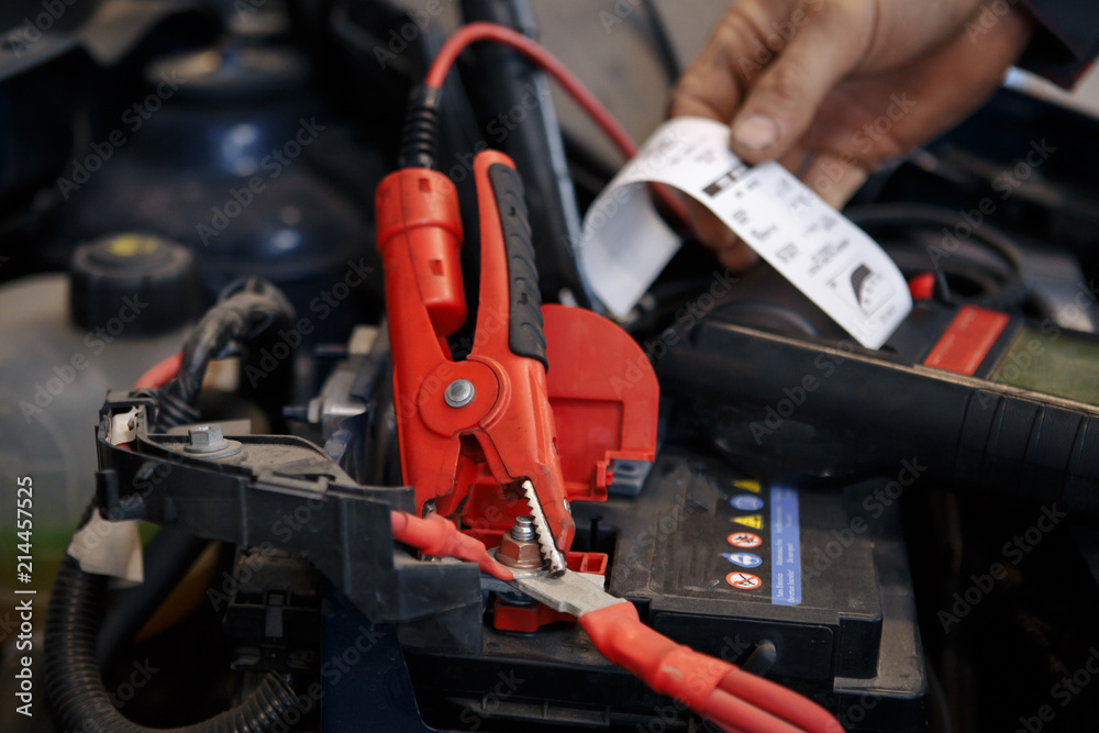 auto mechanic uses multimeter voltmeter to check voltage level in car battery.