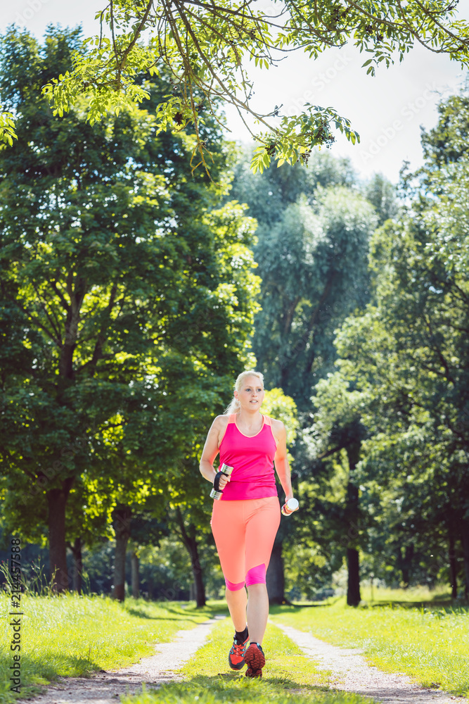 Woman running down a path on grass meadow with weight dumbbells