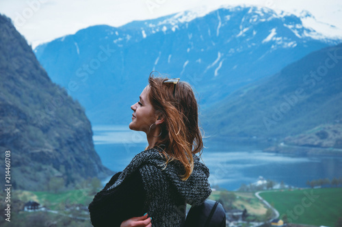 Young woman stands on the background of beautiful mountains and a lake, fjord flam Norway in spring season