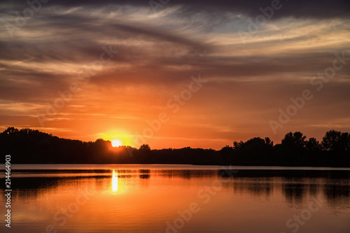 Setting sun over silhouettes of trees with reflection in lake