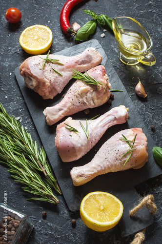 Raw uncooked chicken legs, drumsticks on stone board, meat with ingredients for cooking.