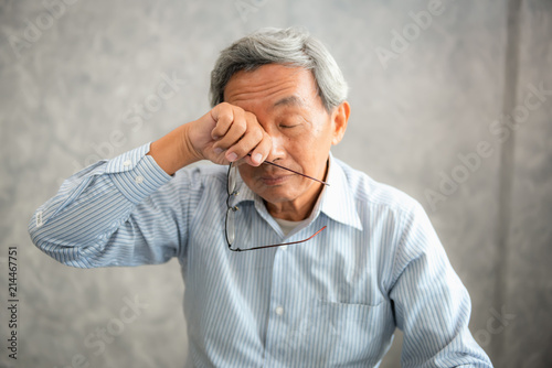 Senior man is holding eyeglasses and  rubbing his tired eyes while reading e-book in tablet photo