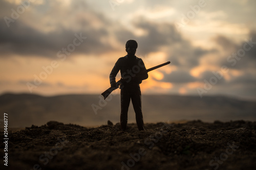 Silhouette of military soldier or officer with weapons at sunset. shot, holding gun, colorful sky, mountain, background. Decoration with toy soldier