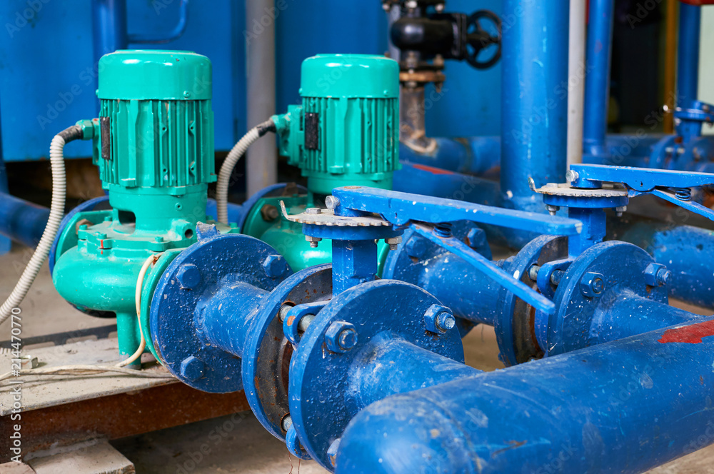Two green electric pump on a water pipeline painted in blue. Industrial background.