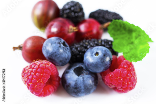 Close-up arrangement mixed, assorted berries including blackberries, strawberry, blueberry, raspberries and fresh leaf on white